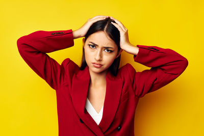 Portrait of young woman with arms crossed against yellow background