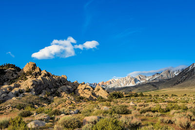 Small puff of white cloud in blue sky above rocky desert plain mountain meadow distant snowy peaks