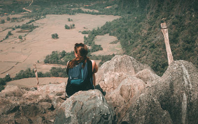 Rear view of woman sitting on rock looking at mountain