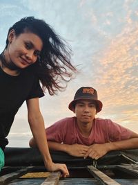 Portrait of couple sitting against sky during sunset