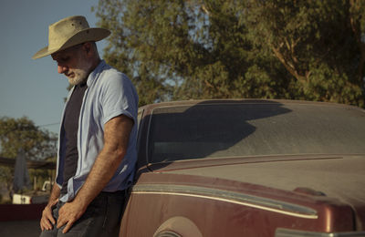 Portrait of adult man in cowboy hat standing against a vintage car