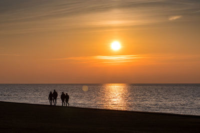 Silhouette people on beach against sky during sunset