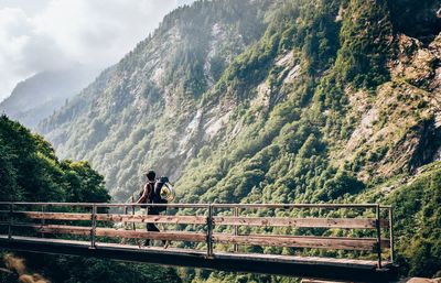 Rear view of hiker walking on bridge against mountains