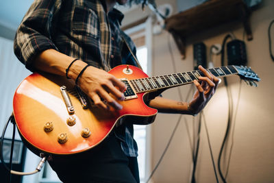 Midsection of man playing guitar while practicing in recording studio