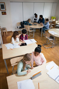 High angle view of students using digital tablet while sitting in classroom