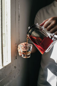 Midsection of man pouring tea in cup by window