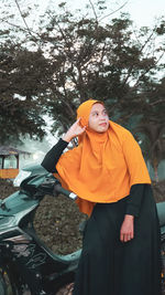 Woman standing by tree against orange sky