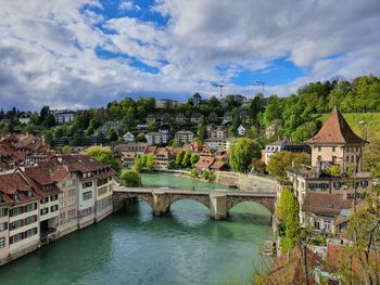 Bridge over river by buildings in town against sky