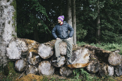 Man sitting on log against trees at forest