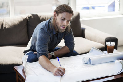 Businessman writing on blueprint in creative office