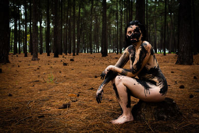 Portrait of naked woman covered with paint while sitting in forest