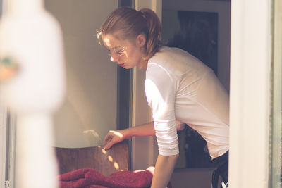 Side view of woman holding chair in brightly lit room