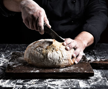 Close-up of person cutting bread with knife at counter