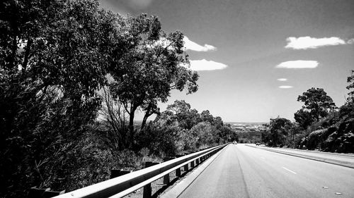 Empty road by trees against sky