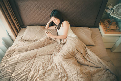 High angle view of mid adult woman using mobile phone while lying on bed at home