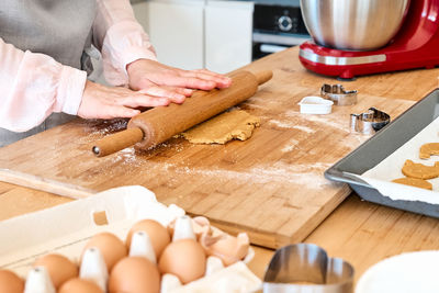 Woman wearing apron baking cookies. housewife flattening dough with rolling pin on the table. 