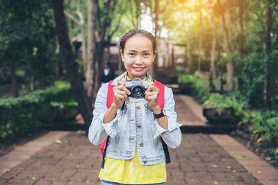 Portrait of smiling girl holding camera while standing outdoors