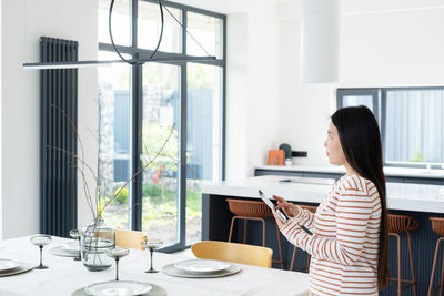 Woman with digital tablet controlling light over dining table modern apartment