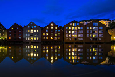 Illuminated buildings by river against sky at night