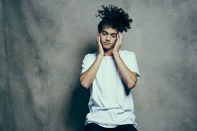 Young man looking away while standing against wall