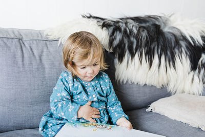 Cute girl reading book while sitting on sofa at home