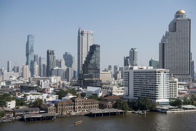 Modern buildings by river against sky in city