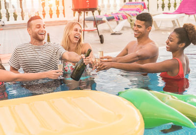 Smiling friends toasting beer bottles and glasses in swimming pool