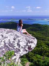 Woman sitting on rock looking at sea against sky