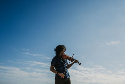 Low angle view of man playing violin against blue sky