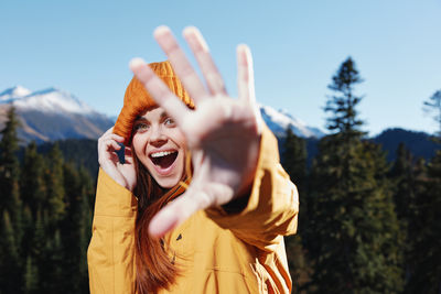 Young woman with arms raised standing against trees