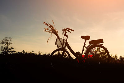 Silhouette bicycle on field against sky during sunset