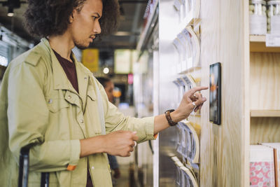 Young male customer using digital tablet mounted on wall at grocery store