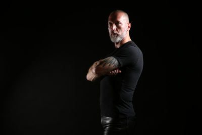 Side view portrait of serious mature man standing against black background