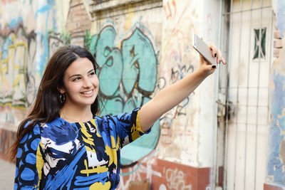 Smiling woman taking selfie by graffiti wall