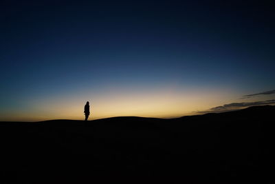 Silhouette man standing on mountain against clear sky during sunset