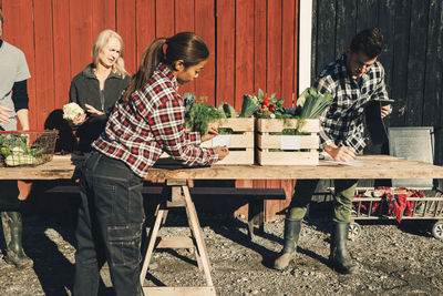 Male and female farmers selling organic vegetables on table outside barn