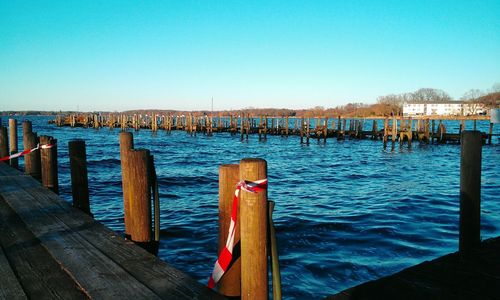 Wooden post on pier at harbor against clear blue sky