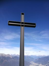 Low angle view of cross on mountains against blue sky