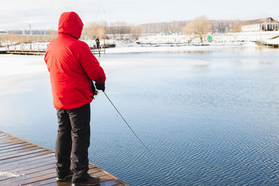 Rear view of man looking at lake during winter