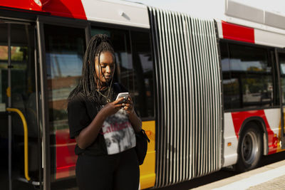 Young woman using cell phone, bus in background