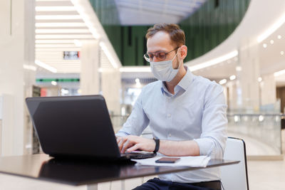Businessman wearing mask working while sitting at mall