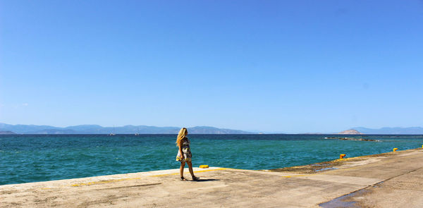 Woman walking at beach against clear blue sky