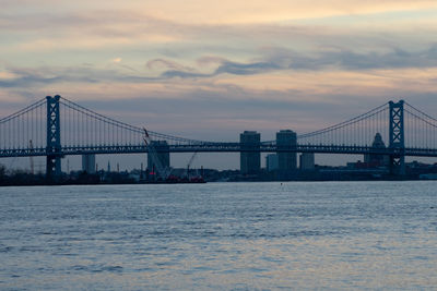 A view of the ben franklin bridge over water on a dramatic sky