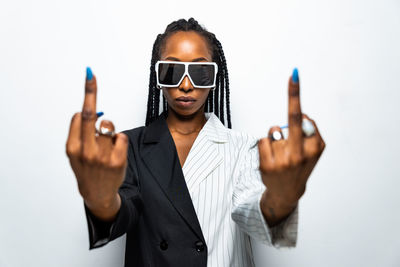 Portrait of young woman wearing sunglasses standing against white background