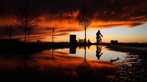 Silhouette person riding bicycle against cloudy sky during sunset
