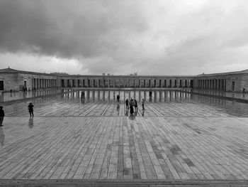 People walking on footpath against cloudy sky