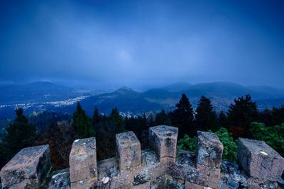 Fortified wall by trees on mountain against blue sky