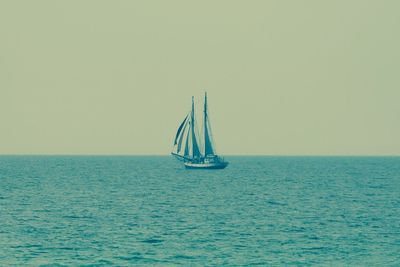 Sailboat sailing in calm sea against clear sky