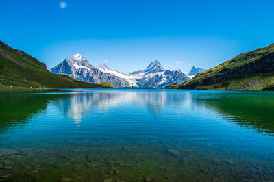 Scenic view of lake and mountains against clear blue sky