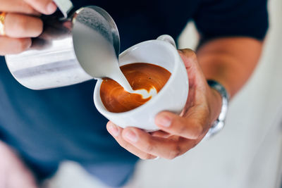 Midsection of man pouring milk in coffee